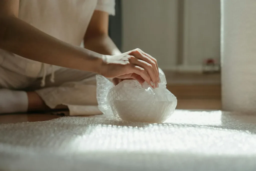 Tangan seseorang membungkus barang dengan bubble wrap untuk persiapan pengiriman
